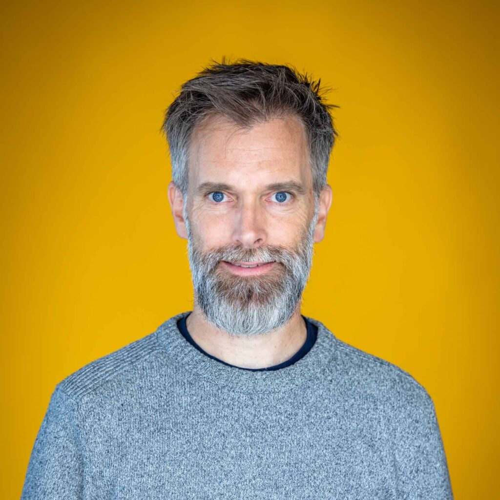 Zu sehen ist das Portrait eines Mannes mit grauem Vollbar vor einer Orangenen Leinwand. Es ist der Fotograf Martin Donat, dem diese Webseite gehört.